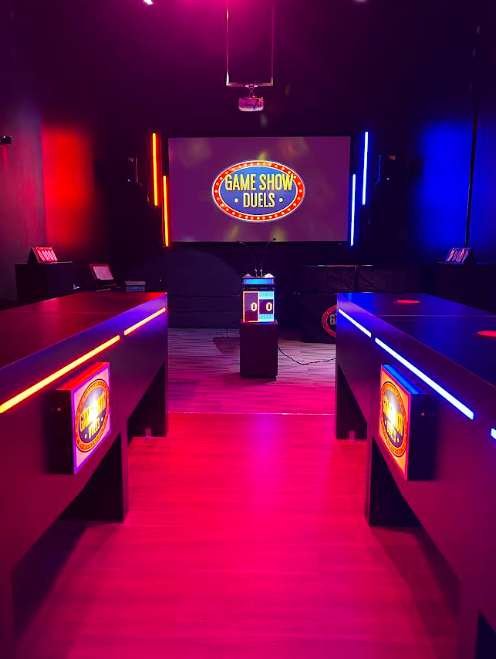 Two lit team lanes face a big screen showing the Game Show Duels logo